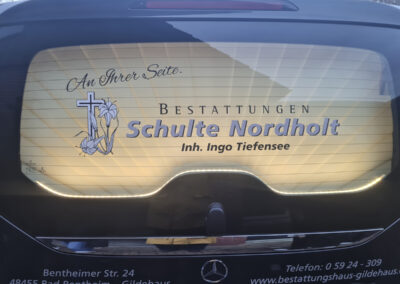 Beleuchtetes Heckfenster des Bestattungsfahrzeugs von Bestattungen Schulte Nordholt mit Firmenlogo, Kontaktdaten und Slogan An Ihrer Seite