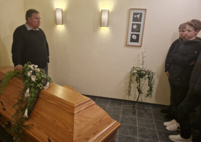 Ingo Tiefensee im Trauerraum des Bestattungshauses Schulte Nordholt während einer Informationsveranstaltung für eine Jugendgruppe vor einem Holzsarg mit Blumenschmuck