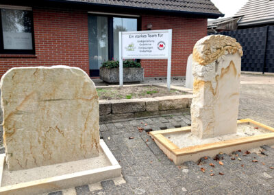 Muster-Grabmale aus hellem Sandstein: Naturbelassener Grabstein und Stele mit Blätterrelief im Außenbereich